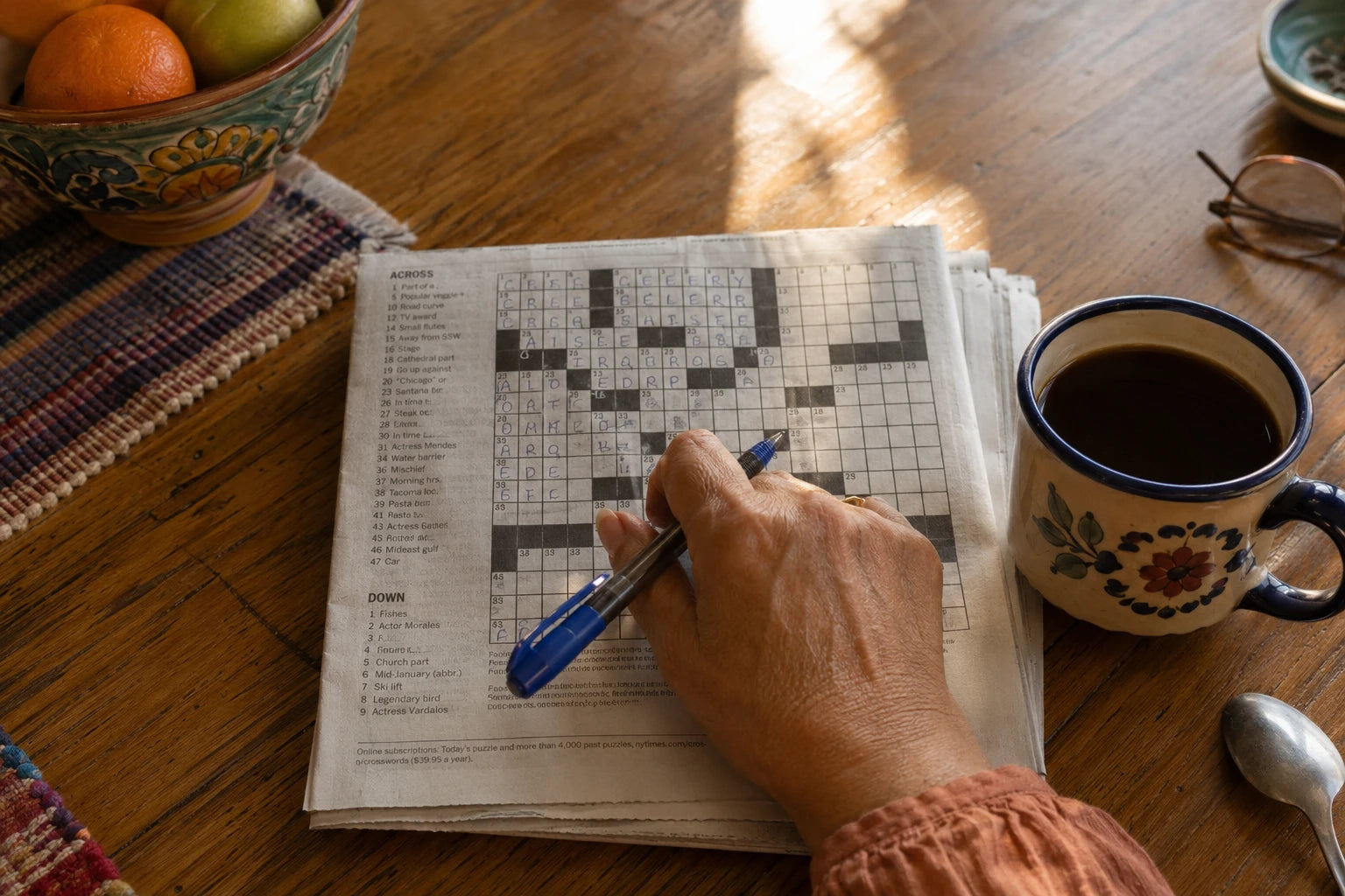 A folded newspaper open at a half-finished crossword on a kitchen table, a woman's hand resting on it holding a pen